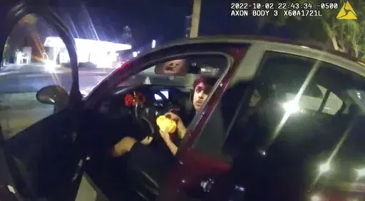 In this image taken from Sunday, Oct. 2, 2022, police body camera video and released by the San Antonio Police Department, Erik Cantu looks toward San Antonio Police Officer James Brennand while holding a hamburger in a fast food restaurant parking lot as the officer opens the car door in San Antonio, Texas. Brennand opened fire several times, wounding the unarmed teenager as he drove away. Brennand was fired after the shooting, and on Tuesday, Oct. 11 he was charged in connection with the shoot
