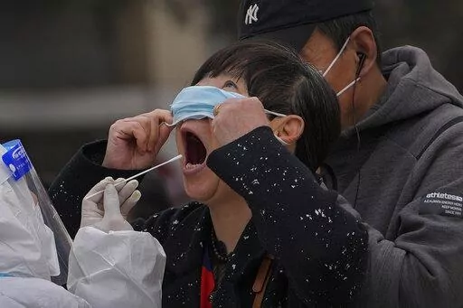 A woman pulls up her mask to get her throat swab at a coronavirus testing site near  residential buildings, Wednesday, April 6, 2022, in Beijing. (AP Photo/Andy Wong)