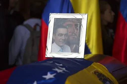 A framed portrait of opposition activist Fernando Alban shadowed by an image of Jesus Christ sits on the flag-draped casket containing his remains, during a solemn ceremony at the National Assembly headquarters, in Caracas, Venezuela, Tuesday, Oct. 9, 2018. A federal judge in Miami has awarded on September 2022,  $73 million in damages to Alban´s family who died while in custody in what he described as a “murder for hire” carried out by a criminal enterprise led by President Nicolas Maduro.