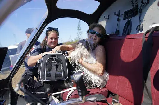 Helen Koch, a dog breeder, is evacuated with some of her 17 dogs on a helicopter for mediccorps.org, who arrived with two helicopters, paramedics and volunteers, in the aftermath of Hurricane Ian on Pine Island, Fla., Saturday, Oct. 1, 2022. The only bridge to the island is heavily damaged so it can only be reached by boat or air. (AP Photo/Gerald Herbert)
