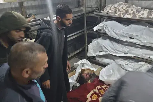 Palestinians stand next to bodies of people killed in an Israeli airstrike in Muwasi, after they were brought to the morgue of a hospital in Khan Younis, Gaza Strip, Wednesday, Dec. 4, 2024. (AP Photo/Mohammad Jahjouh)