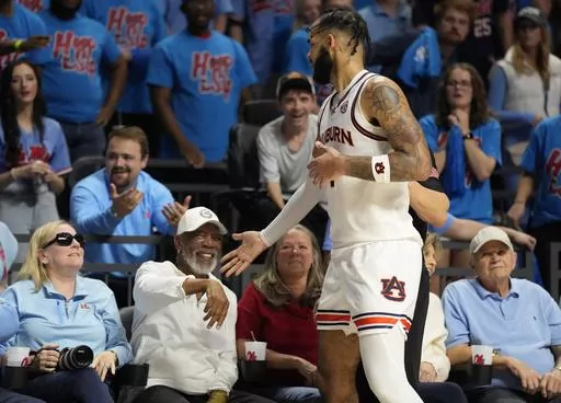 Auburn forward Johni Broome, front right, reaches out and apologizes to Academy Award-winning actor and Mississippi fan Morgan Freeman, second from front left, after falling into him while going after the ball during the second half of an NCAA college basketball game against Mississippi, Saturday, Feb. 3, 2024, in Oxford, Miss. (AP Photo/Rogelio V. Solis)