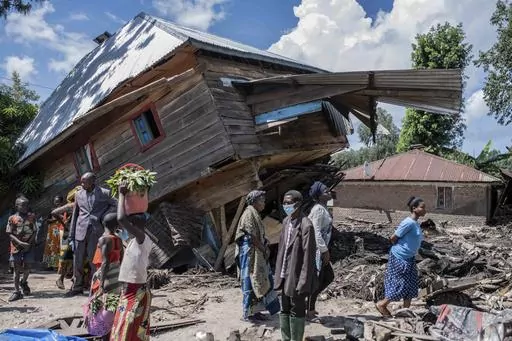 People walk next to a house destroyed by the floods in the village of Nyamukubi, South Kivu province, in Congo, Saturday, May 6, 2023. The death toll from flash floods and landslides in eastern Congo has risen according to the governor and authorities in the country's South Kivu province. (AP Photo/Moses Sawasawa)