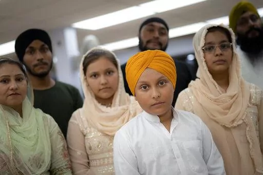 Amandeep Singh, 12, stands with his family in the communal room where "langar," food served after temple services, is provided at Guru Nanak Darbar of Long Island, a Sikh gurdwara, Wednesday, Aug. 24, 2022, in Hicksville, N.Y. Their Afghan Sikh family of 13 has found refuge in the diaspora community on Long Island where the Sikh community is helping family members obtain work permits, housing, healthcare and find schools for the children. (AP Photo/John Minchillo)