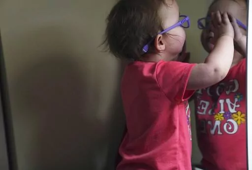 The Hackneys’ daughter looks at her reflection in a bedroom mirror during a supervised visit at her parent's home in Oakdale, Pa., on Thursday, Nov. 17, 2022. At 8 months old, the young child was taken from her parents custody after arriving at the hospital severely dehydrated and malnourished. The Hackneys and their lawyer believe the Allegheny County Family Screening tool may have flagged the couple as dangerous because of their disabilities. (AP Photo/Jessie Wardarski)