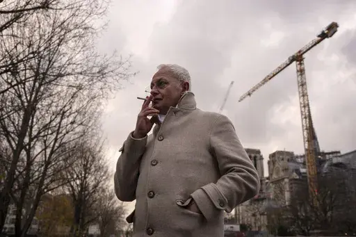 Notre-Dame de Paris cathedral chief architect Philippe Villeneuve smokes a cigarette by the cathedral during an interview with Associated Press, Tuesday, Dec. 3, 2024 in Paris. (AP Photo/Louise Delmotte)