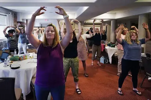 CORRECTS INSTRUCTORS NAME TO EMILY DANIELS FROM EMILY RILEY Instructor Emily Daniels, left, raises her arms while leading a workshop helping teachers find a balance in their curriculum while coping with stress and burnout in the classroom, Tuesday, Aug. 2, 2022, in Concord, N.H. School districts around the country are starting to invest in programs aimed at address the mental health of teachers. Faced with a shortage of educators and widespread discontentment with the job, districts are hiring m