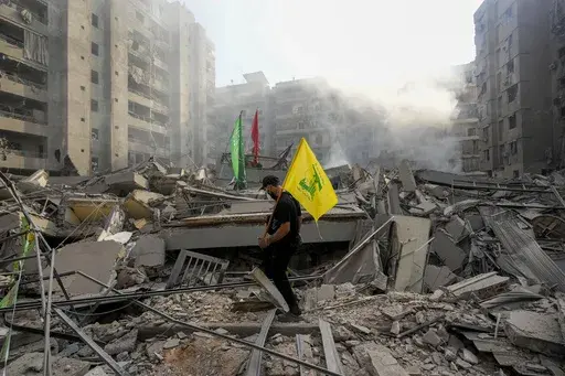 A man carries a Hezbollah flag as he walks on the rubble of his destroyed apartment following an Israeli airstrike in Lebanon, Nov. 1, 2024. (AP Photo/Hassan Ammar, File)