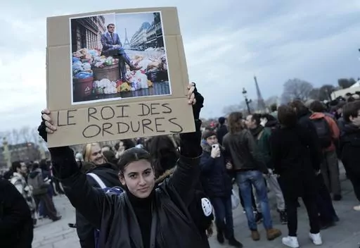 A woman holds a placard depicting French President Emmanuel Macron sitting on garbage cans that reads, "king of trash" during a protest in Paris, Friday, March 17, 2023. Protests against French President Emmanuel Macron's decision to force a bill raising the retirement age from 62 to 64 through parliament without a vote disrupted traffic, garbage collection and university campuses in Paris as opponents of the change maintained their resolve to get the government to back down. (AP Photo/Lewis Jol