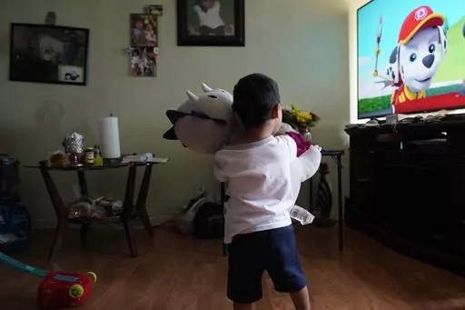 Alexander, 3, who is being treated for developmental delays, holds a stuffed animal and watches Paw Patrol in the living room of his West Chicago, Ill., home Tuesday, Aug. 8, 2023. Alexander qualified for five Early Intervention therapies in summer 2021, physical, occupational, developmental, behavioral and speech when he was about a year old. But the family waited more than a year to get any of these services in-person. (AP Photo/Charles Rex Arbogast)