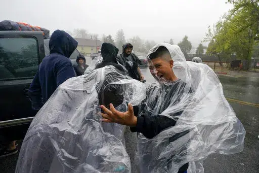 Members of the Ornelas family put on plastic raincoats as wind and rain pummel the area Friday, Sept. 9, 2022, in Julian, Calif. A tropical storm nearing Southern California has brought fierce mountain winds, high humidity, rain and the threat of flooding to a region already dealing with wildfires and an extraordinary heat wave. (AP Photo/Gregory Bull)